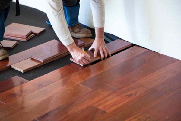 A person marking a piece of hardwood flooring during installation.